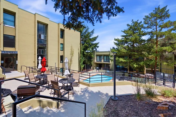 Exterior property featuring a swimming pool, multiple outdoor seating areas, mature trees, and a building entrance with "LOBBY" signage