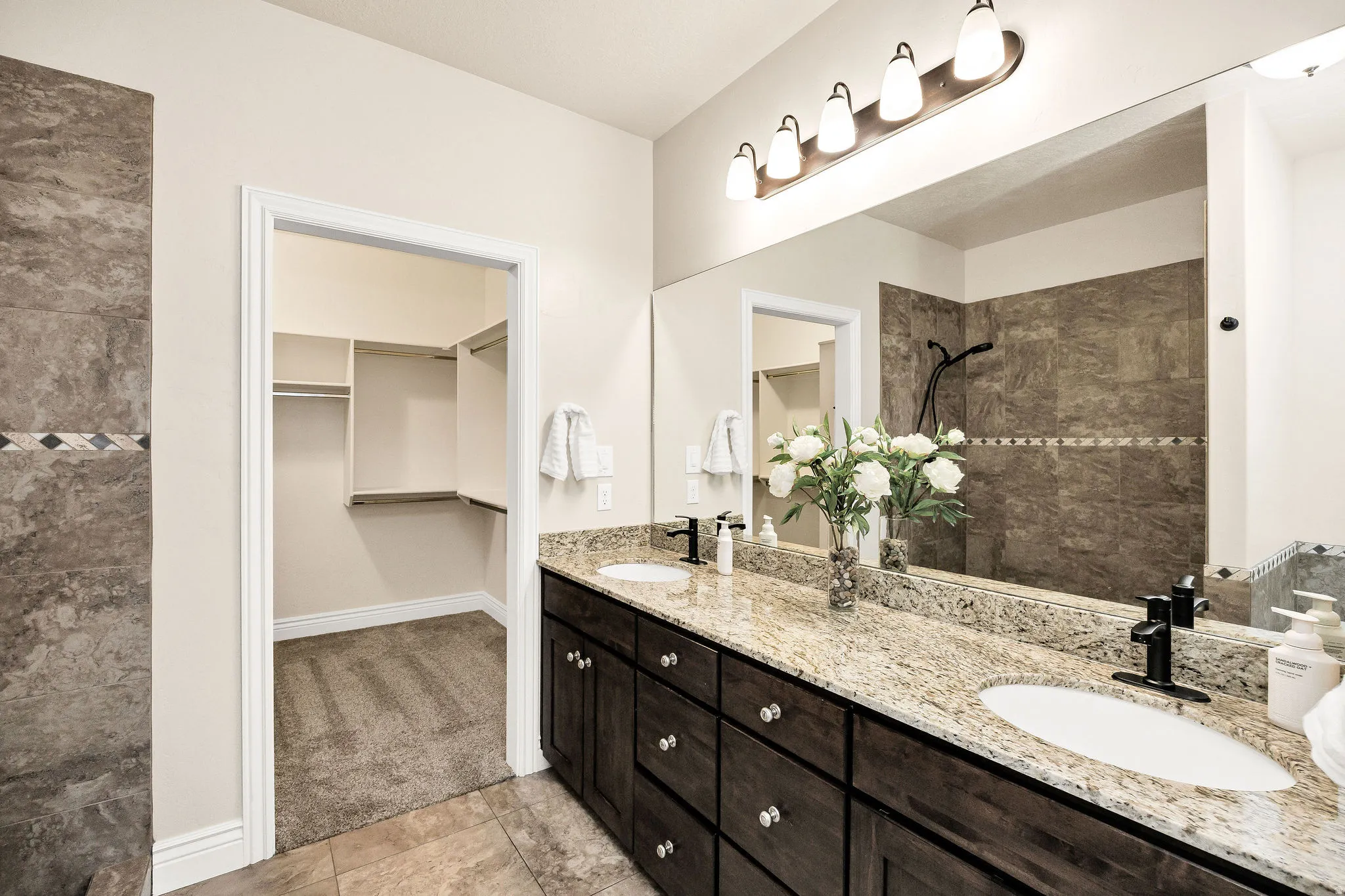 Primary bathroom vanity featuring dual sinks, granite countertops, dark wood cabinetry, and matte black fixtures