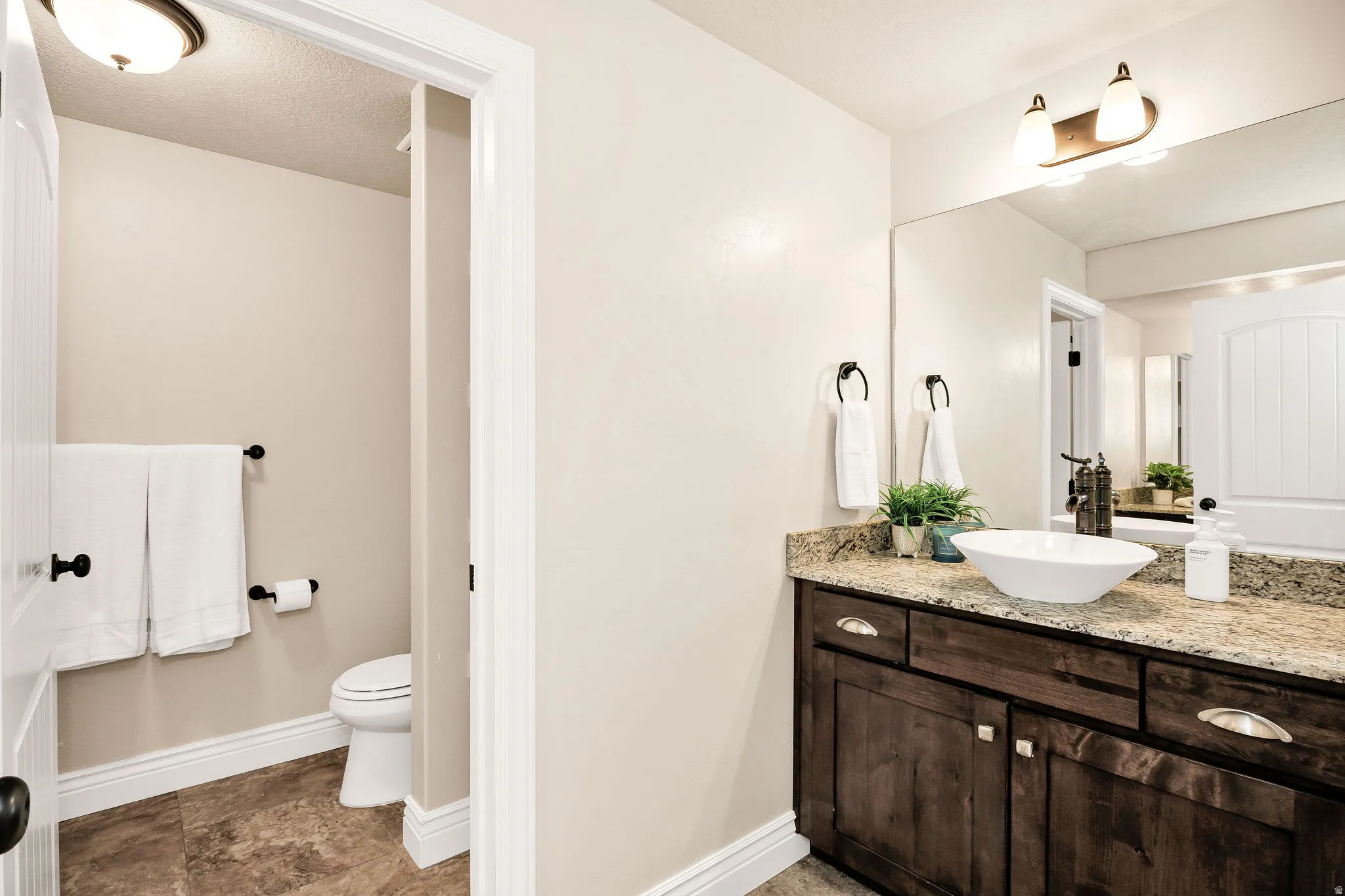 Bathroom vanity featuring a vessel sink, stone countertop, wood-finish cabinetry, and an expansive wall mirror