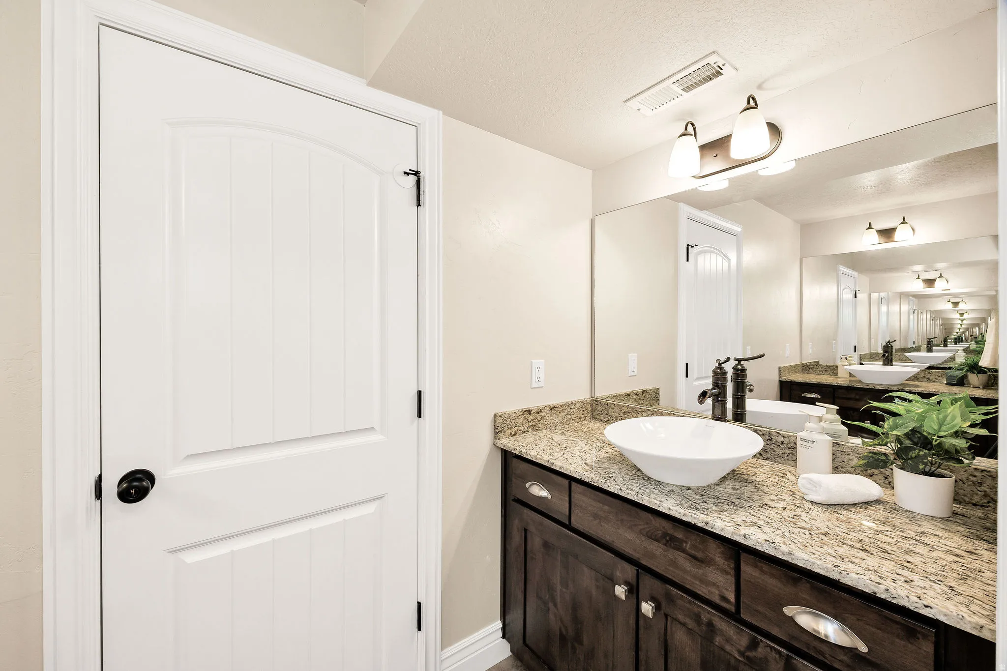 Bathroom vanity featuring a vessel sink, dark wood cabinetry with chrome pulls, and a granite countertop