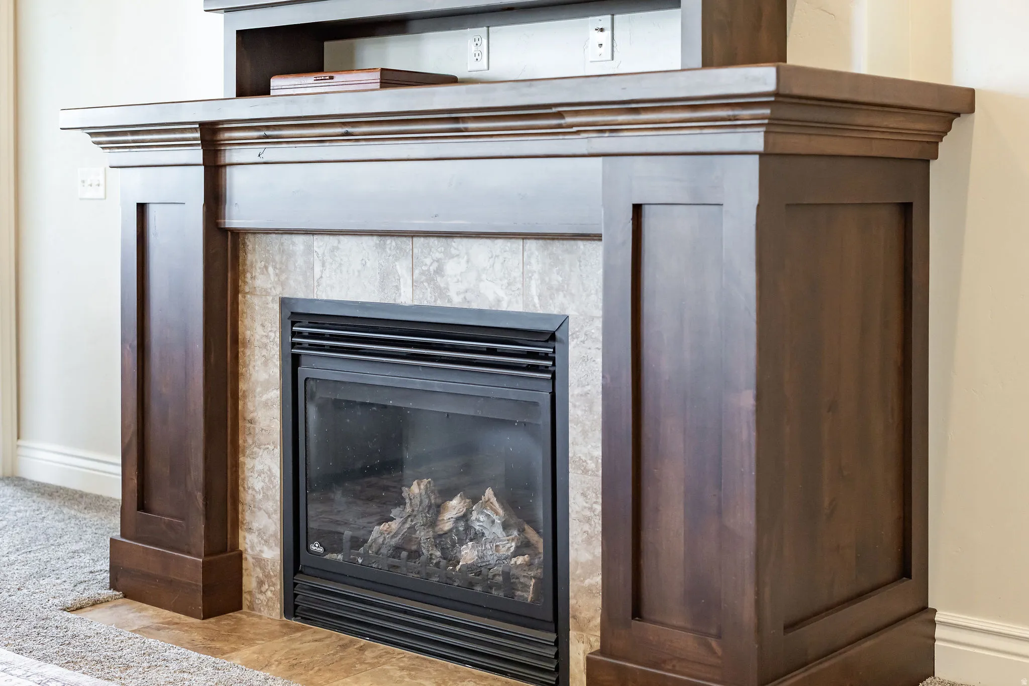 Wood-finish fireplace with a tiled surround, black firebox, and decorative gas logs