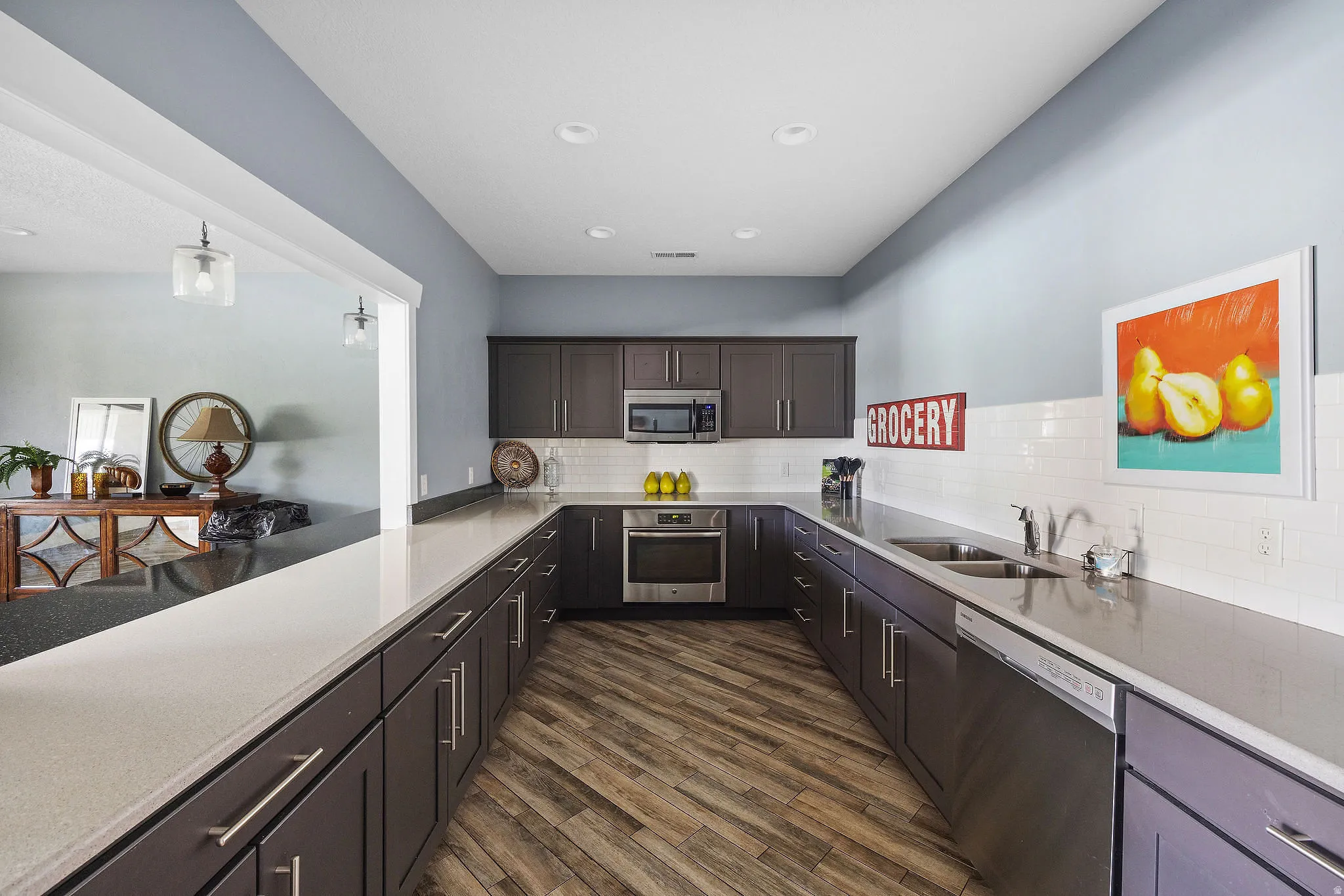 Clubhouse Kitchen featuring dark wood cabinetry, light-toned countertops, wood-finish flooring, stainless steel appliances, and a white subway tile backsplash