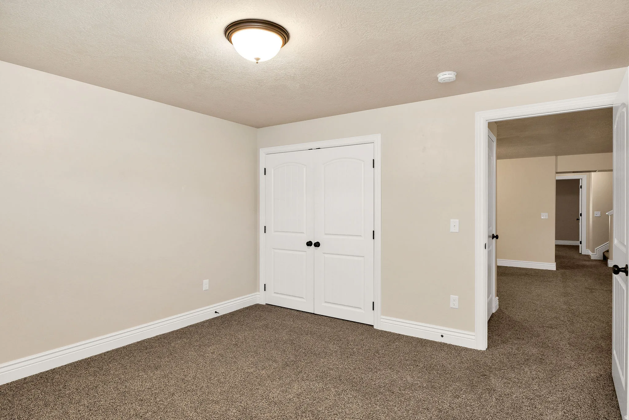 Neutral-toned wall paint with white trim, brown carpet flooring, and a white double bifold door