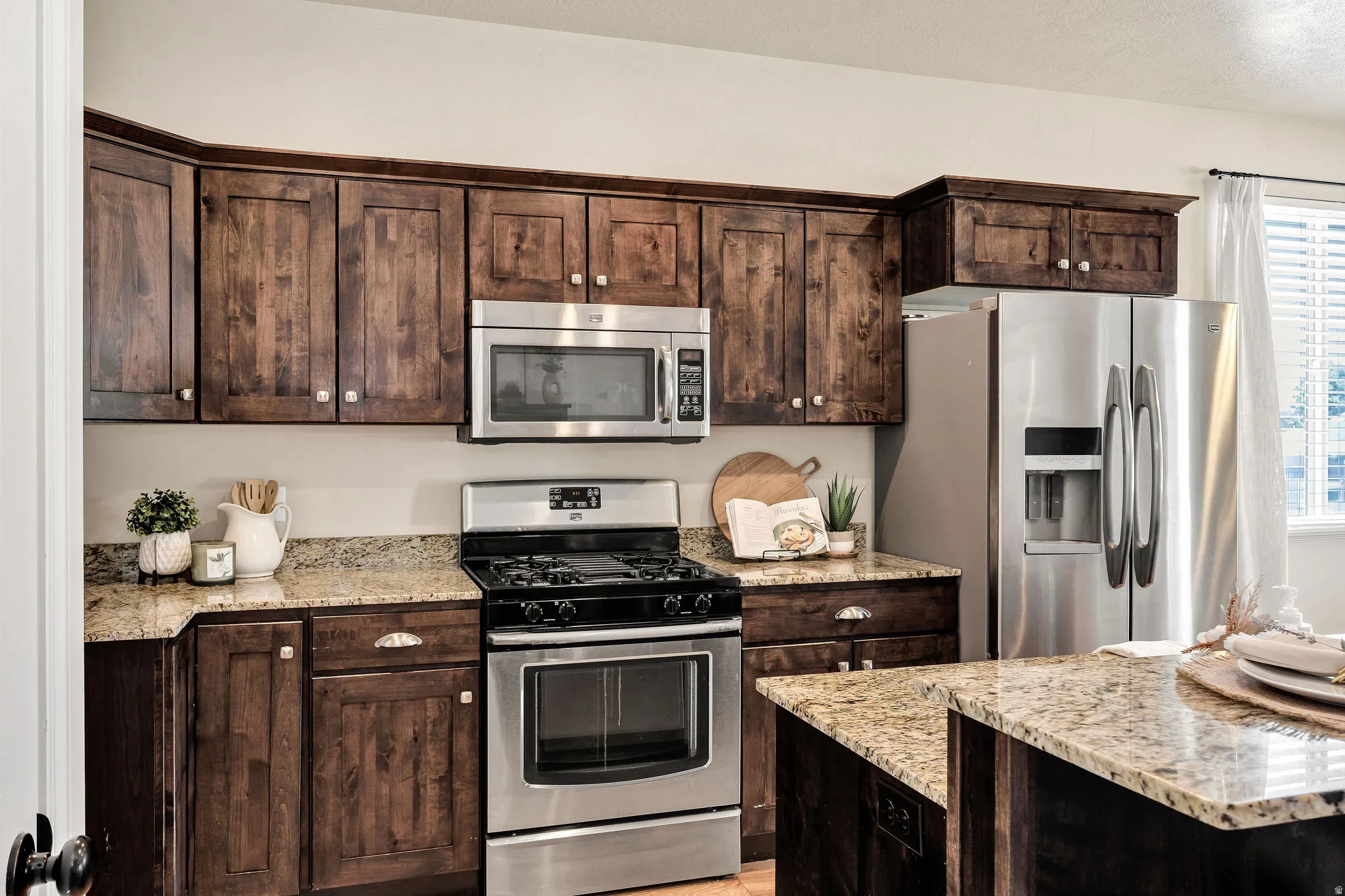 Kitchen featuring wood-finish cabinetry, granite countertops, and stainless steel appliances including a range, built-in microwave, and side-by-side refrigerator