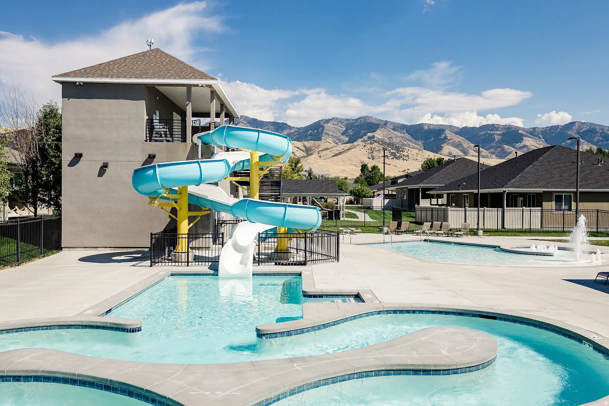 Outdoor aquatic area featuring multiple pools, a water slide structure, a fountain feature, and surrounding concrete decking