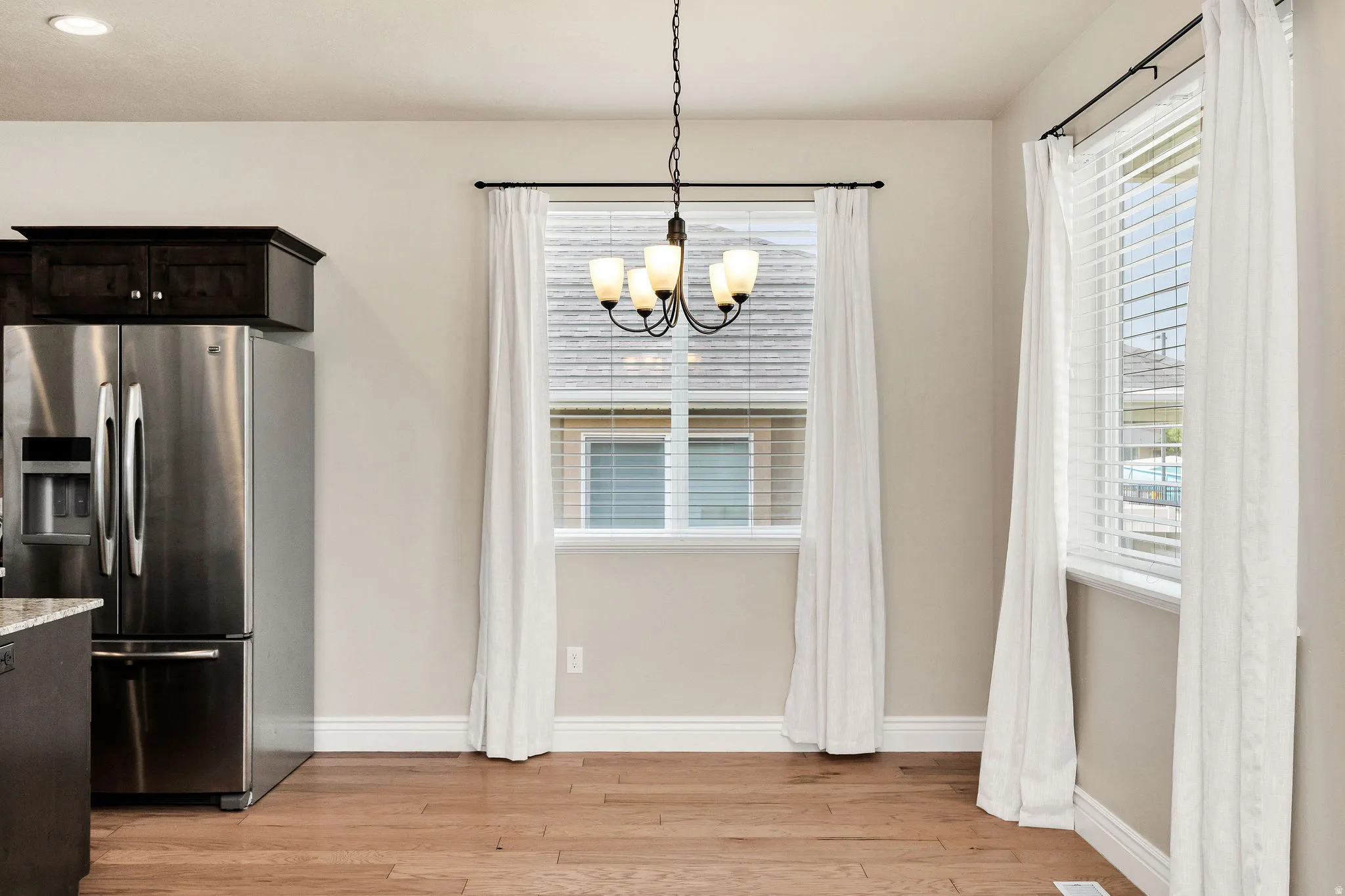 Bright dining space featuring wood-finish flooring, a contemporary chandelier, two windows with blinds, and recessed lighting