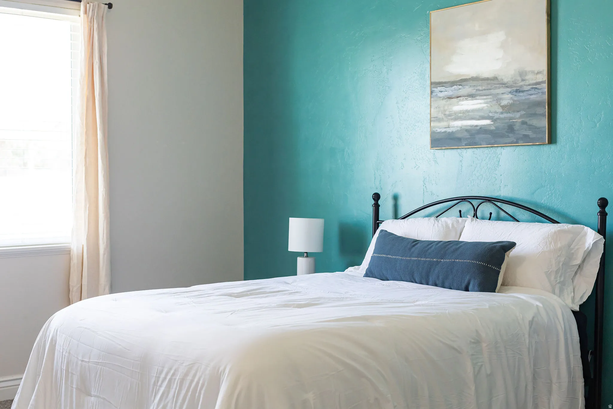 Primary bedroom featuring a window with blinds, light-colored curtains, textured accent wall, and a black metal headboard