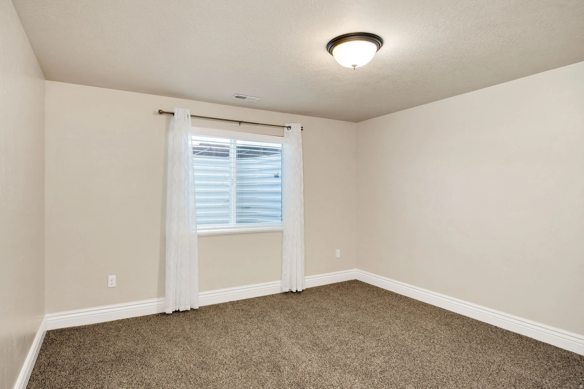 Carpeted interior room featuring light beige walls, white baseboards, and a white-framed window