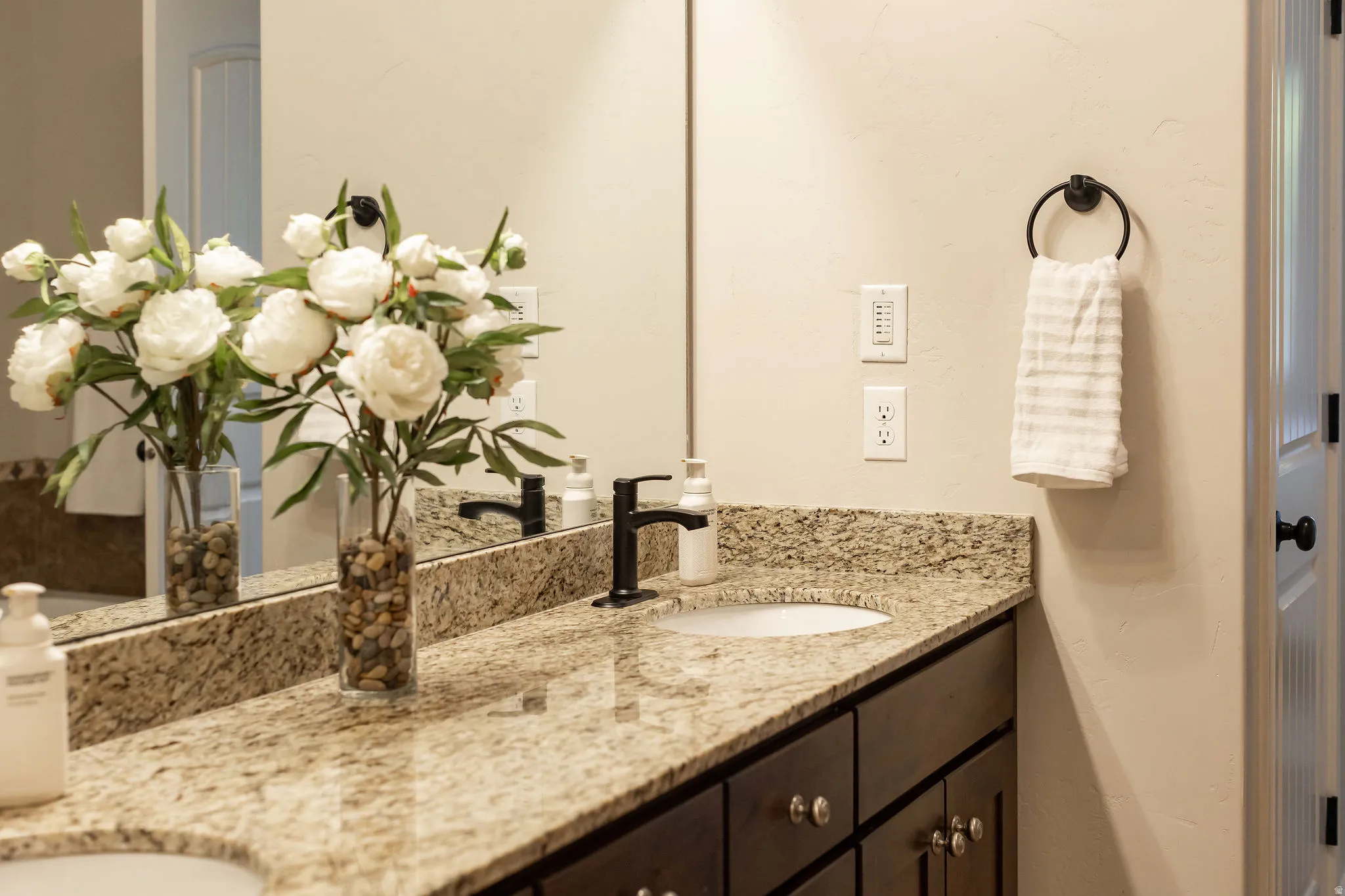 Dual vanity with a light-toned granite-style countertop, dark wood cabinetry, and matte black fixtures