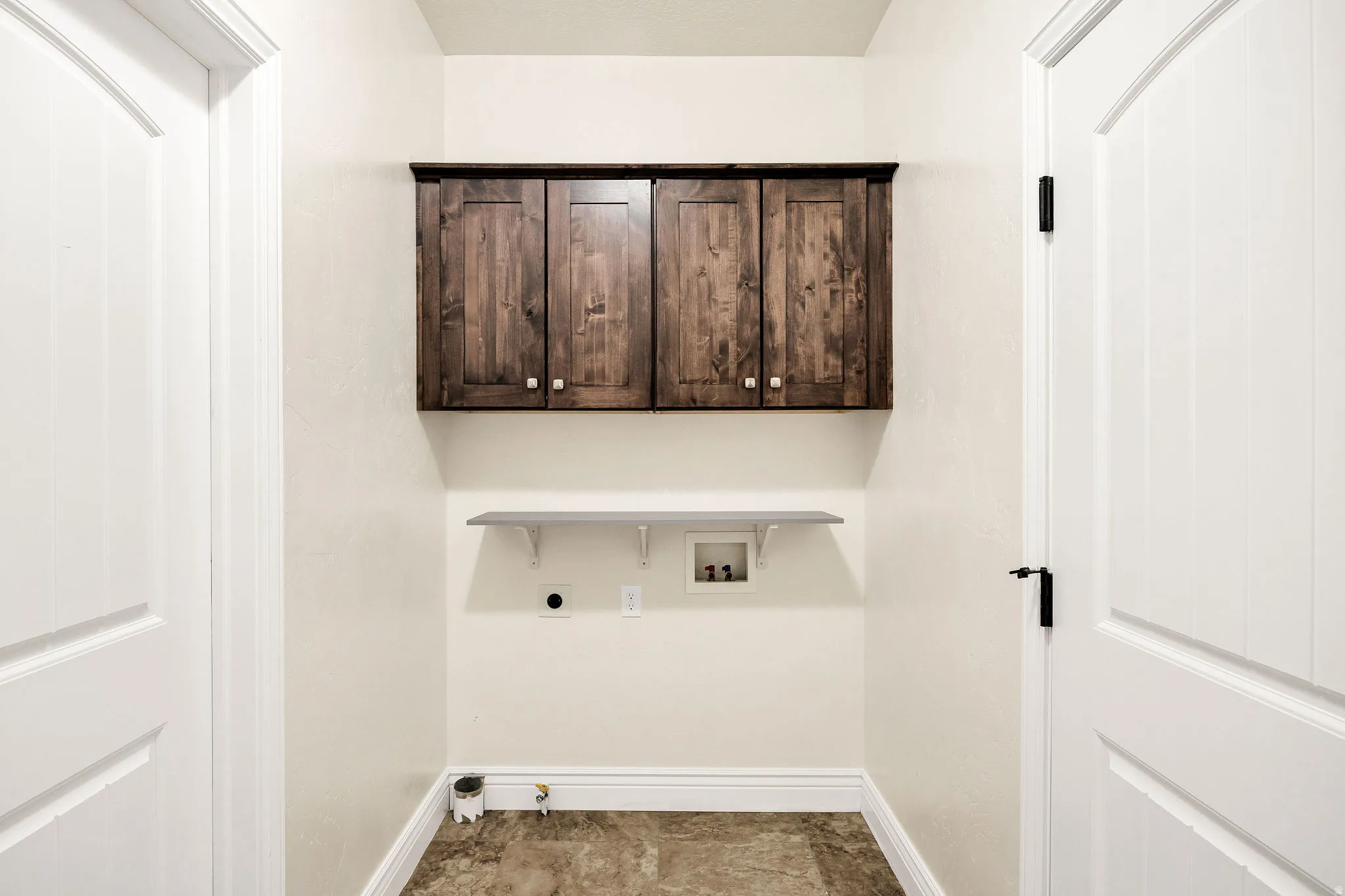 Laundry area with wood-finish upper cabinetry, a white floating shelf, and neutral-toned flooring