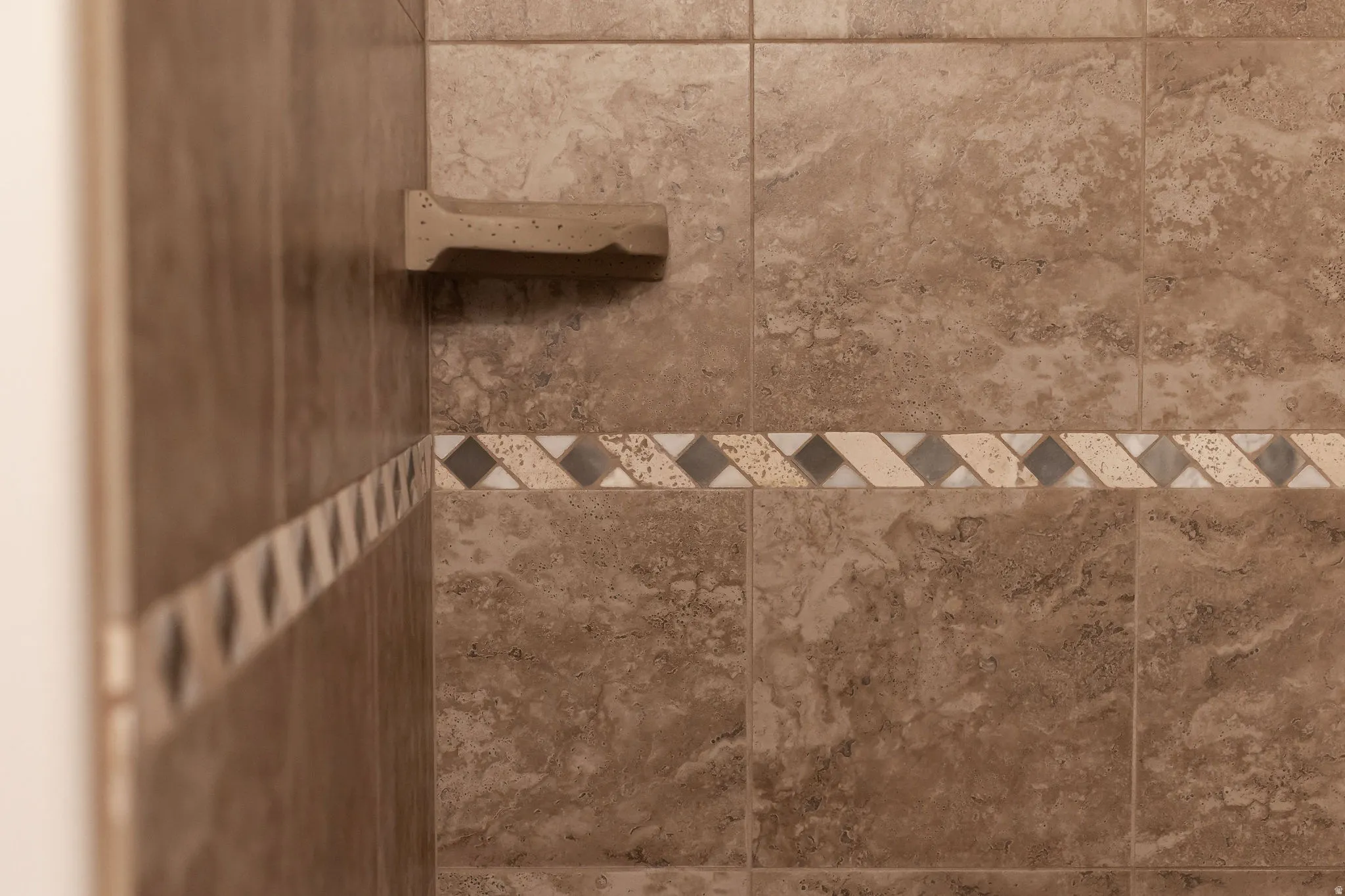 Tiled shower surround featuring a decorative accent band and an integrated soap dish