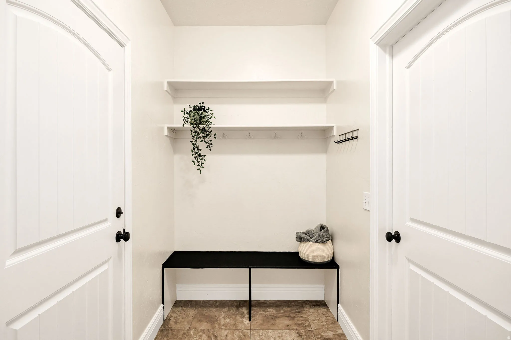 Tiled flooring entryway featuring a built-in bench, two wall-mounted shelves, and integrated coat hooks