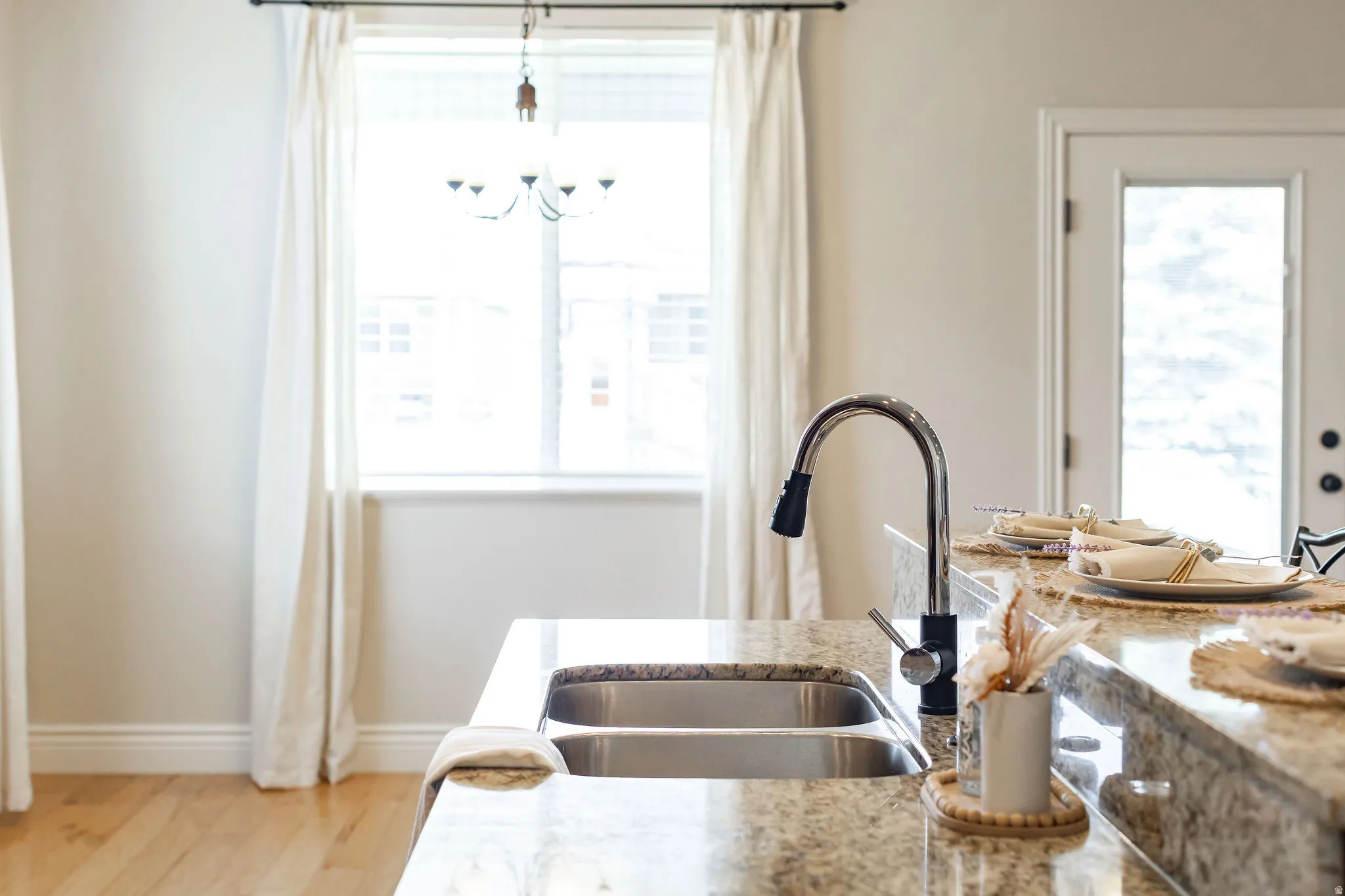 Kitchen island featuring a double basin stainless steel sink with a high-arch pull-down faucet, a granite-finish countertop, and wood-finish flooring
