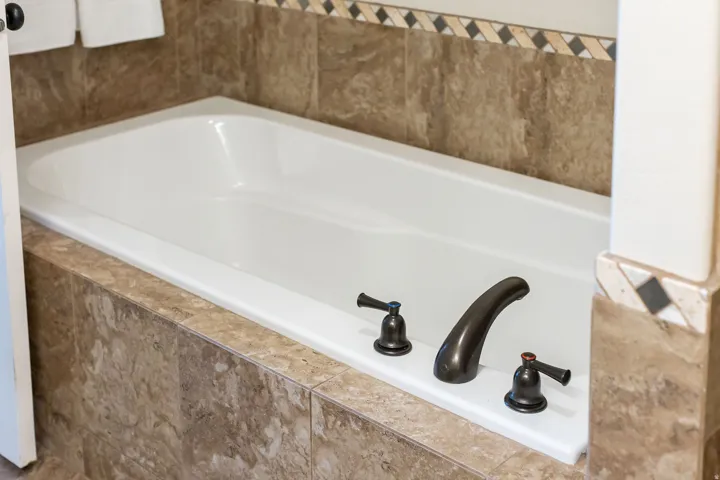 White built-in bathtub featuring a stone tile surround, decorative accent tile border, and oil-rubbed bronze fixtures