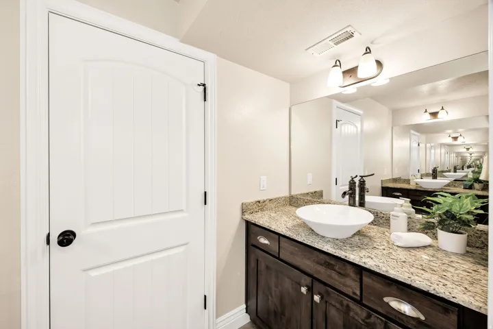 Bathroom vanity featuring a vessel sink, dark wood cabinetry with chrome pulls, and a granite countertop