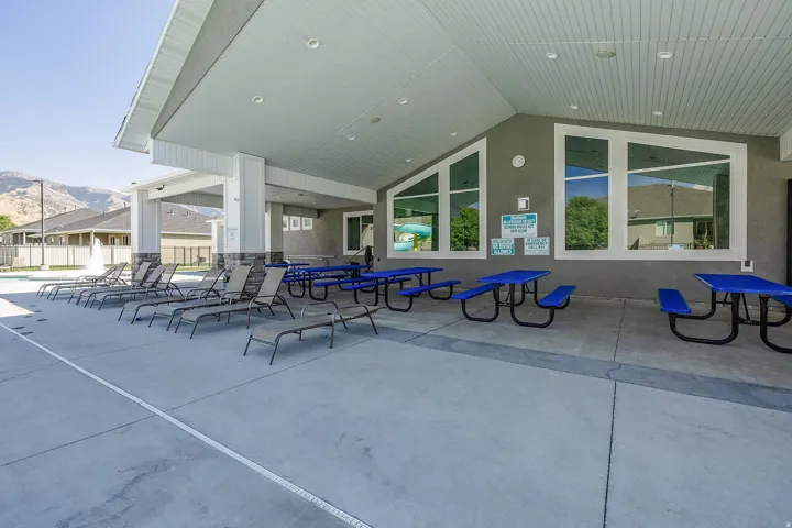 Outdoor covered patio area featuring concrete flooring, recessed lighting, white columns with stone-finish bases, and multiple expansive windows
