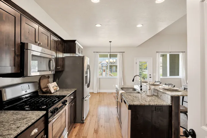 Kitchen featuring dark wood cabinetry, stainless steel appliances, granite countertops, a kitchen island with a double sink, and wood-finish flooring