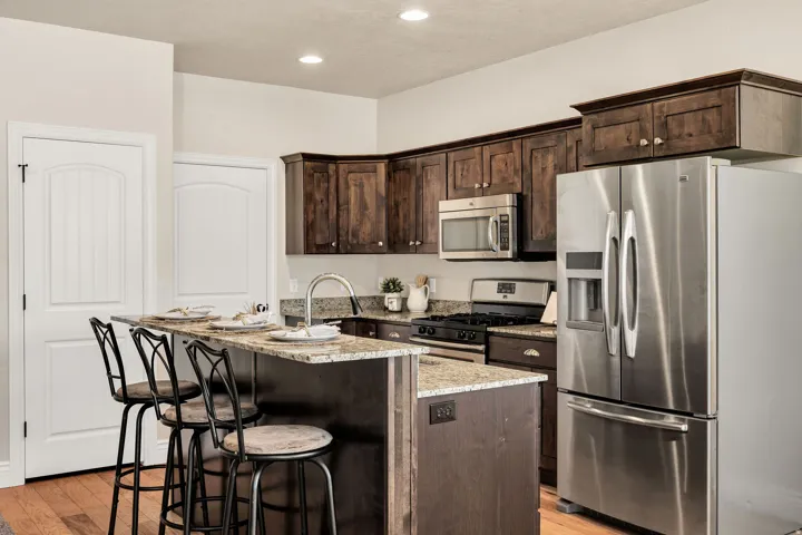 Kitchen featuring dark wood cabinetry, stainless steel appliances, a gas range, and a breakfast bar with granite-finish countertops