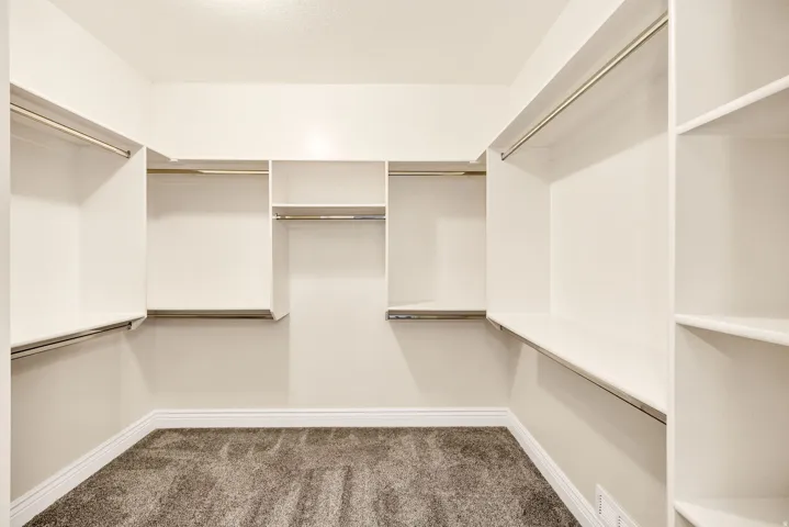 Primary walk-in closet featuring built-in shelving, multiple hanging rods, and plush carpeting