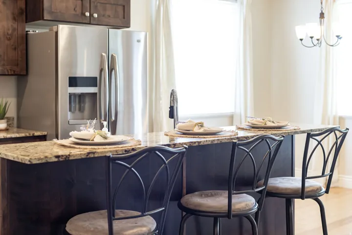 Kitchen island featuring a granite countertop with a dark wood-finish base, stainless steel refrigerator, and dark wood-finish upper cabinetry