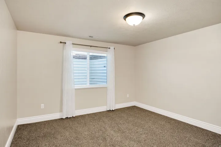 Carpeted interior room featuring light beige walls, white baseboards, and a white-framed window