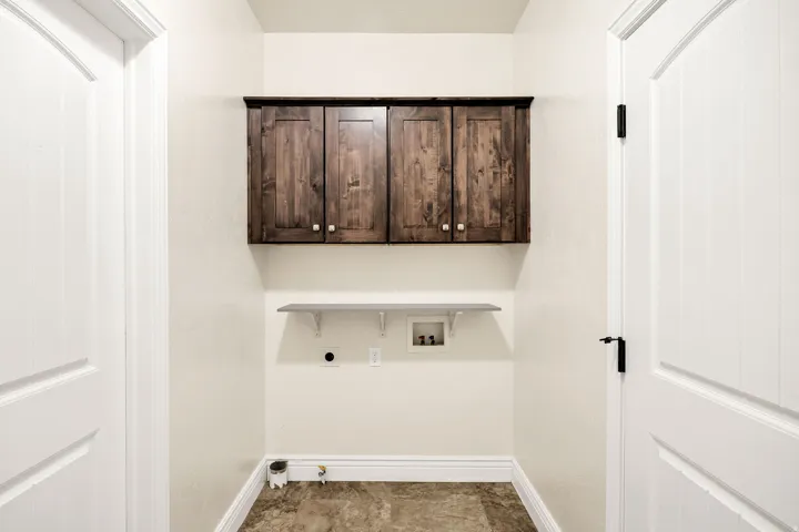 Laundry area with wood-finish upper cabinetry, a white floating shelf, and neutral-toned flooring