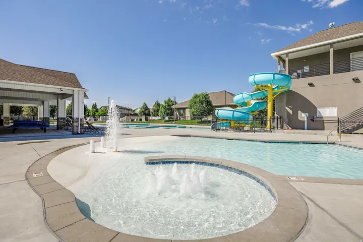 Community swimming pool featuring a water slide, splash pad with water features, and a covered pavilion