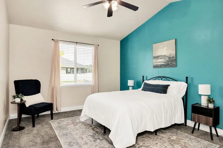 Vaulted ceiling primary bedroom with a vibrant accent wall, ceiling fan, and window with blinds