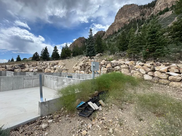 Concrete foundation walls and slab, surrounded by natural rock retaining walls and mature evergreen trees