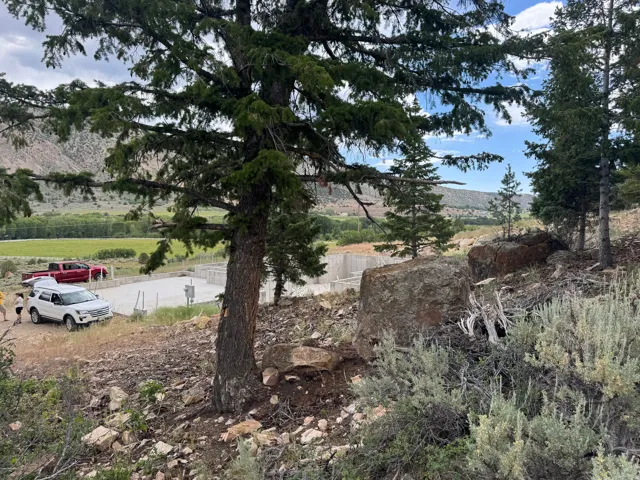 Concrete foundation pad with utility hookups, established trees, natural rock formations, and surrounding vegetation
