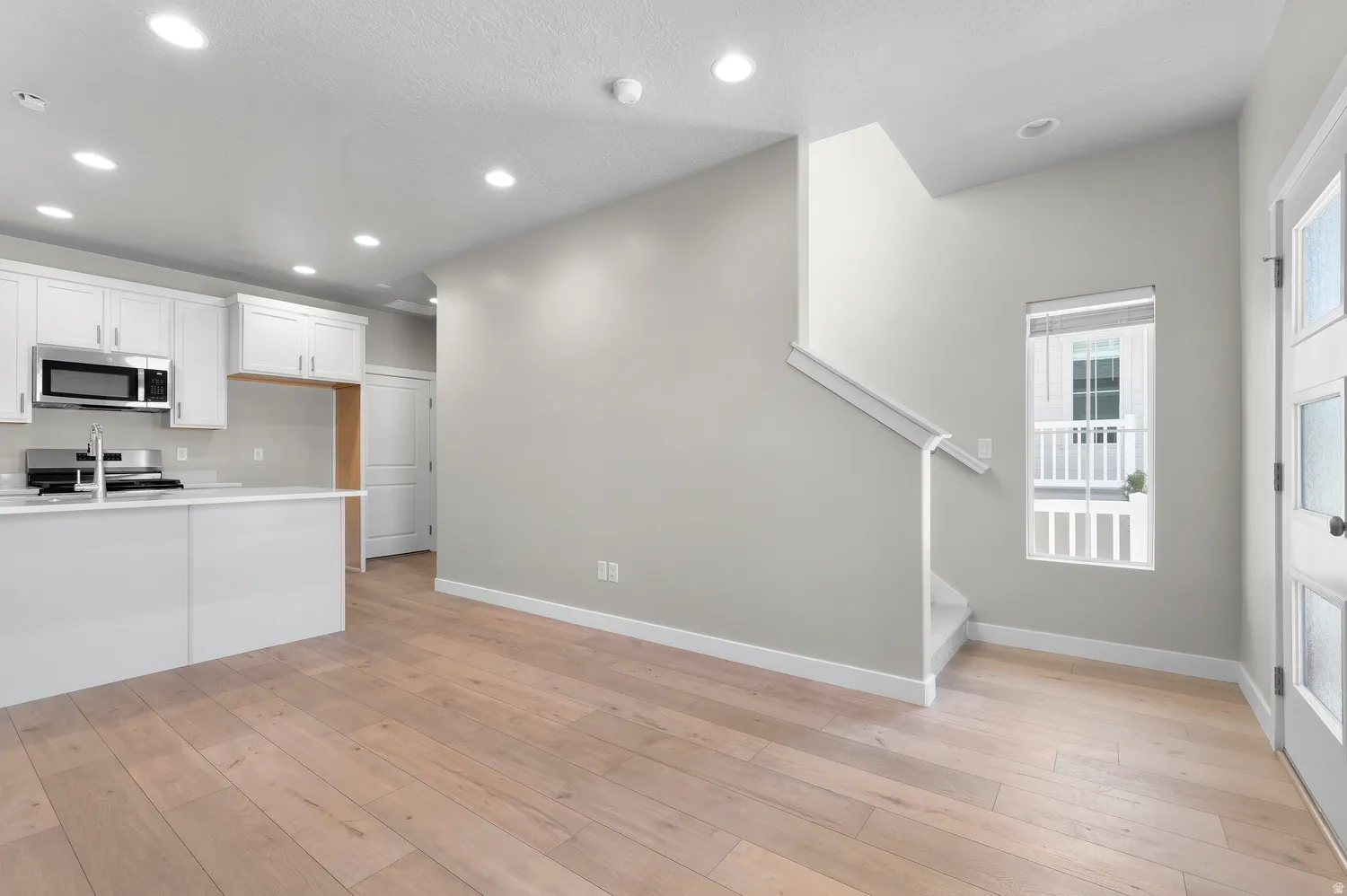 Hardwood-finish flooring, recessed lighting, white kitchen cabinetry, stainless steel microwave, and a white front door with decorative glass panels