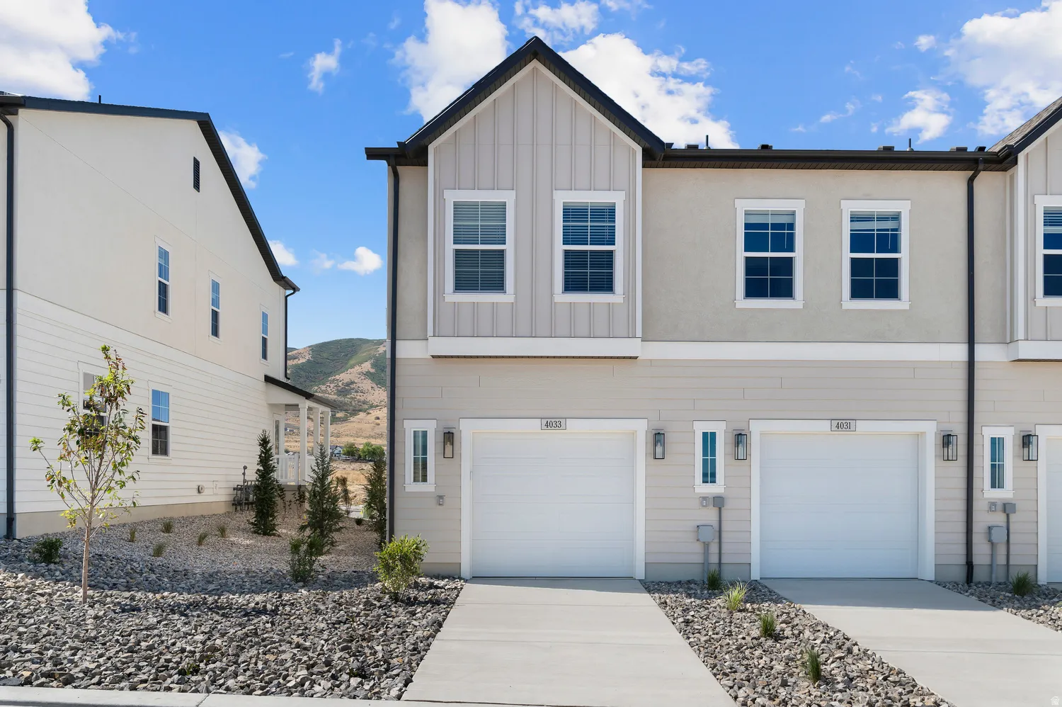 Contemporary townhome exterior featuring an attached two-car garage, concrete driveway, and rock landscaping