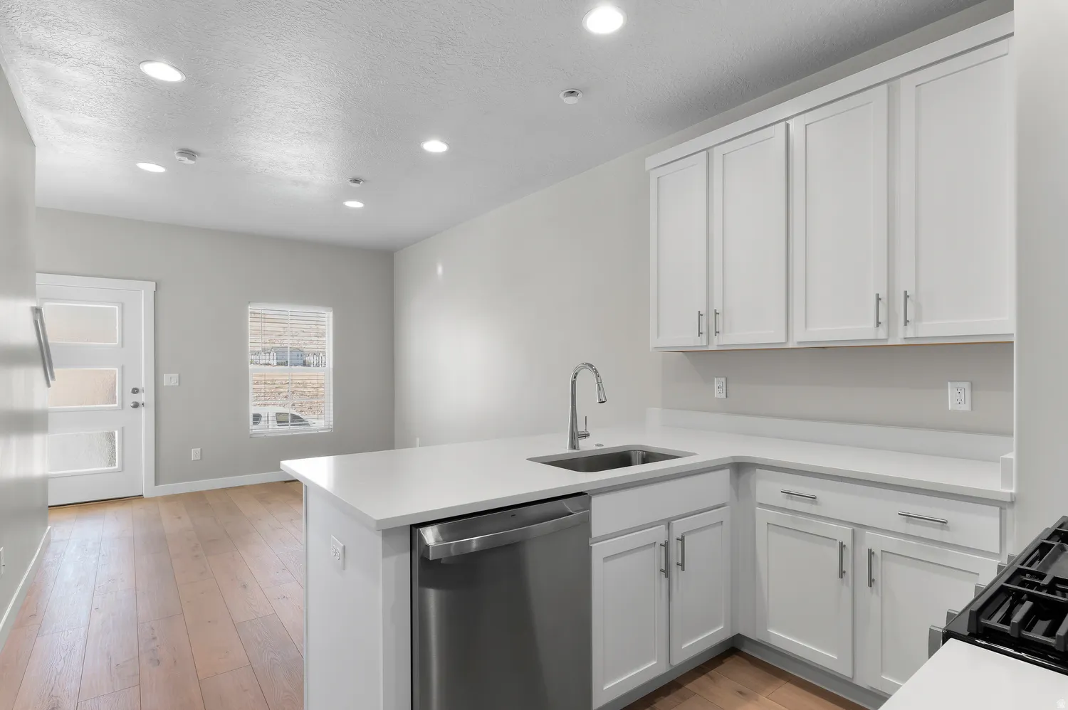 Kitchen featuring white cabinetry, stainless steel dishwasher, undermount sink with a gooseneck faucet, light-toned countertops, and wood-finish flooring