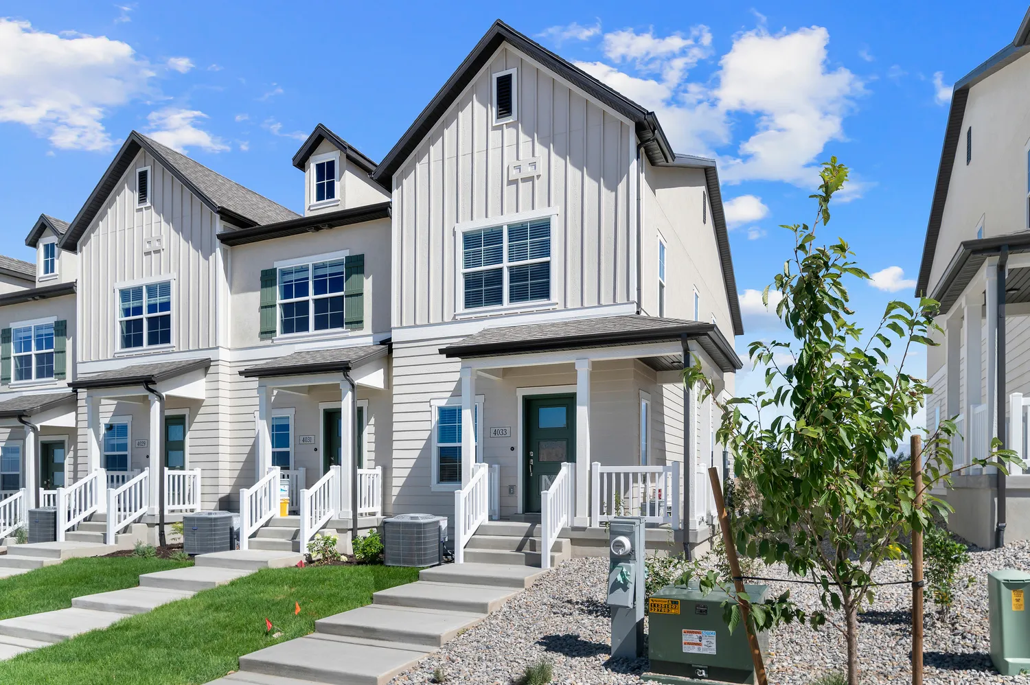 Modern townhome exterior featuring light-colored siding, a covered front porch, and a dormer window