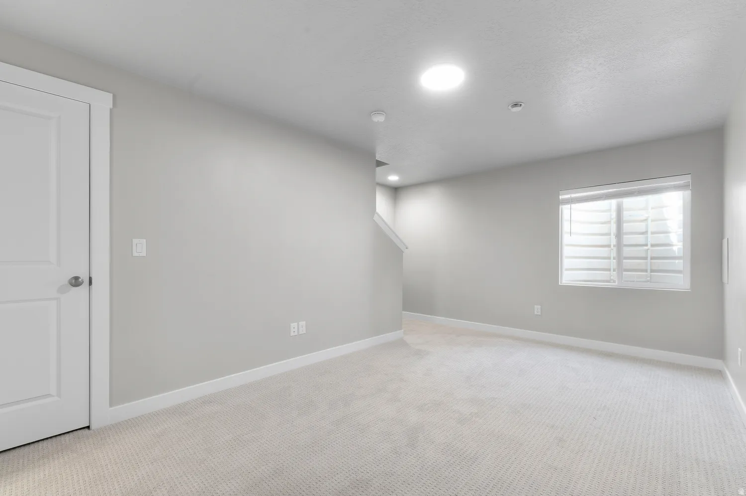 Neutral-toned walls, recessed ceiling lighting, light-colored carpeting, white trim, and a window with white shutters