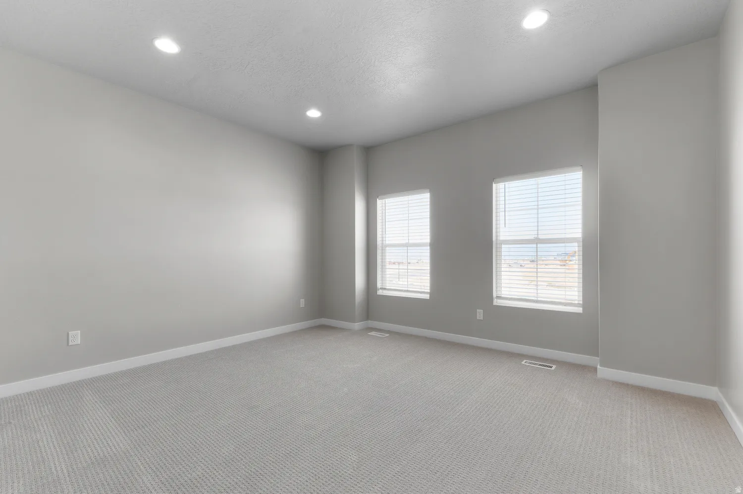 Recessed lighting illuminates this carpeted room featuring two windows with horizontal blinds