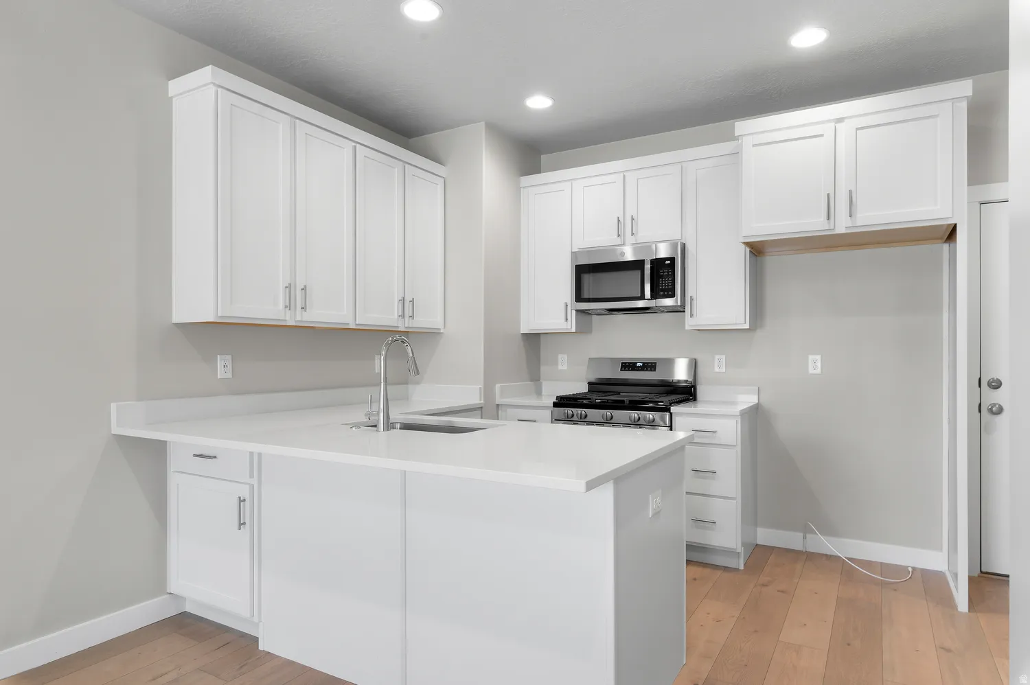 Kitchen featuring white cabinetry, light-toned countertops, a stainless steel microwave, a stainless steel gas range, and wood-finish flooring