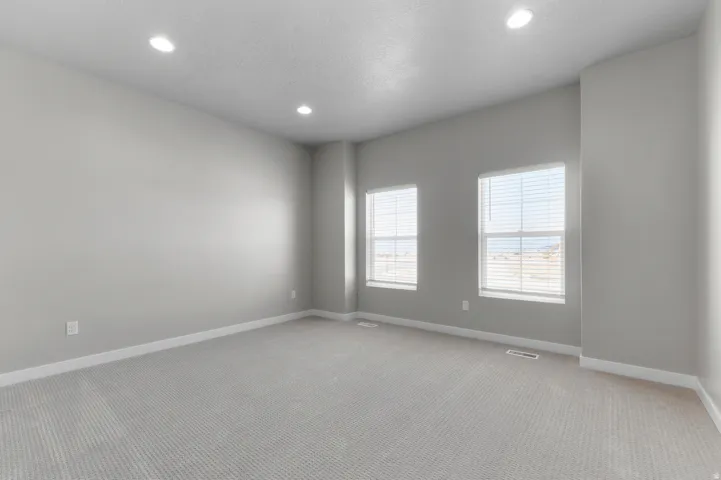 Recessed lighting illuminates this carpeted room featuring two windows with horizontal blinds