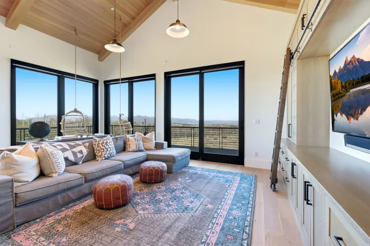 Vaulted ceiling with wood-finish planks, large black-framed windows, built-in entertainment center with storage, light wood-finish flooring, and pendant lighting fixtures