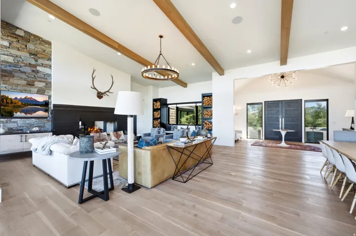 Spacious living area featuring light wood-finish flooring, exposed ceiling beams, and a stone accent wall with built-in fireplace