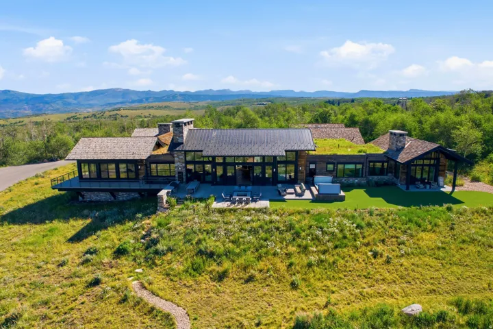 Modern mountain residence featuring a stone and wood exterior, expansive glass-paneled walls, multiple outdoor patio spaces, and a distinctive green roof