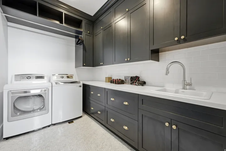 Laundry room featuring extensive dark cabinetry with gold-toned hardware, white countertops, and a white subway tile backsplash