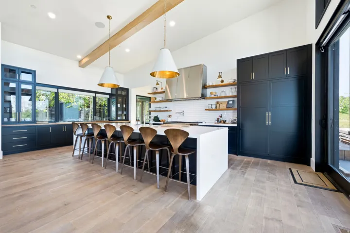 Spacious kitchen featuring an oversized island with seating, extensive dark cabinetry, wood-finish flooring, a white subway tile backsplash, and stainless steel appliances