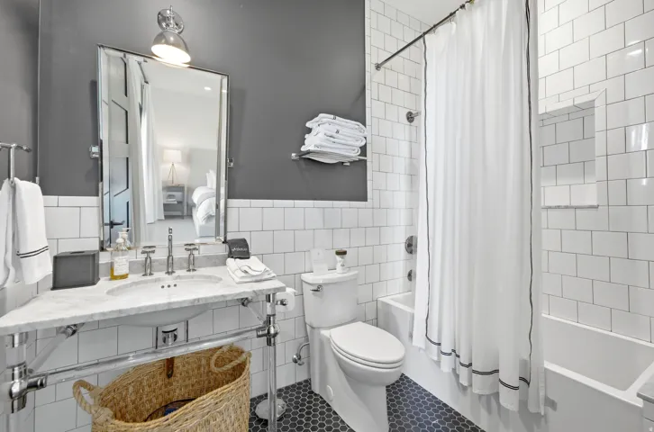 Bathroom featuring white subway tile, a chrome vanity with a marble-finish countertop, a single basin sink with chrome fixtures, a toilet, and a combination tub/shower with a built-in niche