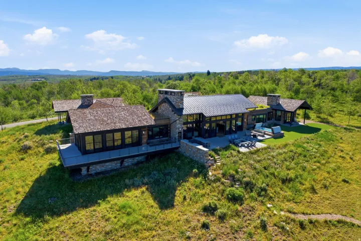 Expansive modern residence featuring stone and wood siding, multiple outdoor patios, and a contemporary architectural design