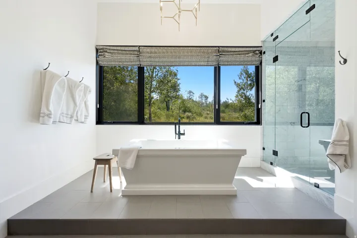 Freestanding soaking tub with a modern floor-mounted faucet, complemented by a large window with a patterned roller shade