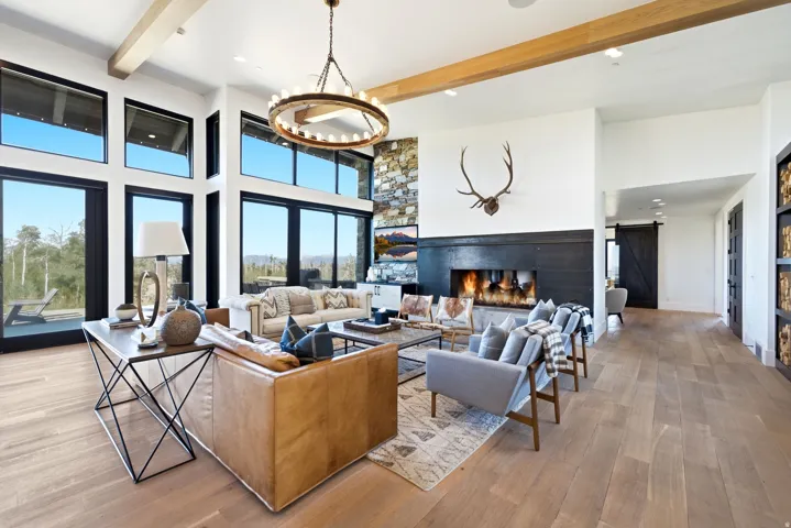 Great room featuring a full-height stone accent wall, a linear gas fireplace with a dark wood mantel, and expansive floor-to-ceiling windows