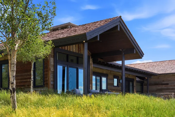 Rustic wood-sided exterior featuring extensive glazing, a covered patio, and a shingle roof