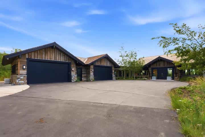 Expansive paved driveway leading to a multi-car garage with black doors