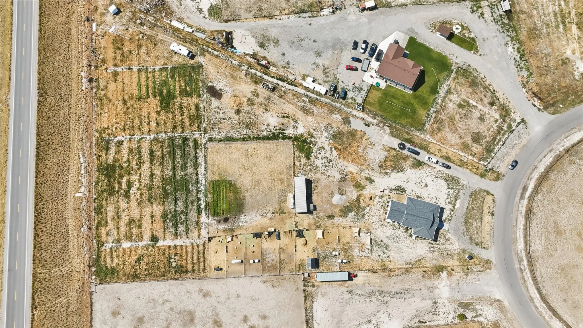Aerial view of a property featuring two distinct residential structures, agricultural plots, and multiple outbuildings